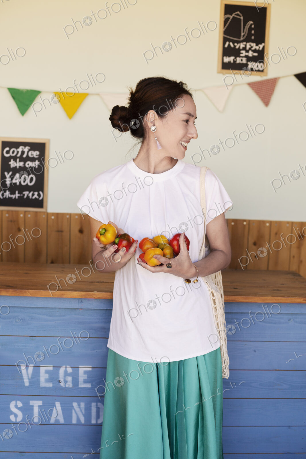 Smiling Japanese woman standing in a farm shop, holding vegetables.