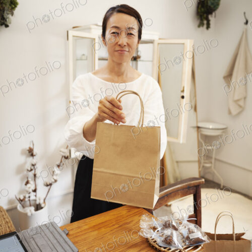 Smiling Japanese woman standing in a small fashion boutique, holding brown paper… Smiling Japanese woman standing in a small fashion boutique, holding brown paper…