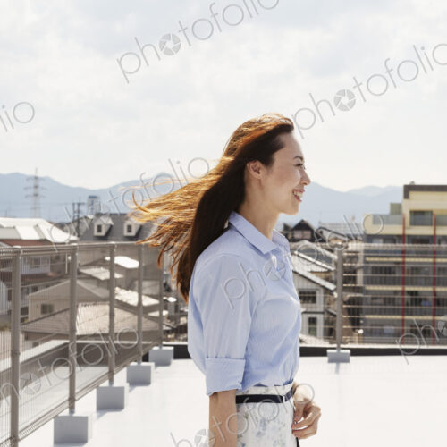 Smiling Japanese woman standing on a rooftop in an urban setting. Smiling Japanese woman standing on a rooftop in an urban setting.