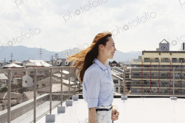 Smiling Japanese woman standing on a rooftop in an urban setting.