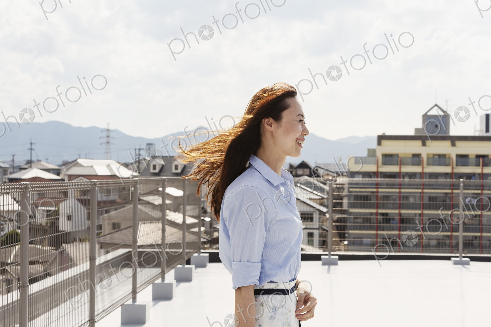 Smiling Japanese woman standing on a rooftop in an urban setting.