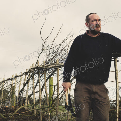 Smiling bearded man holding axe and bill hook standing next to a newly built… Smiling bearded man holding axe and bill hook standing next to a newly built…