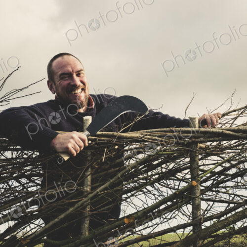 Smiling bearded man holding bill hook standing next to a newly built traditional hedge. Smiling bearded man holding bill hook standing next to a newly built traditional hedge.