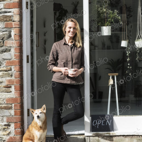 Smiling female owner of plant shop standing outside her store, a dog sitting next to her. Smiling female owner of plant shop standing outside her store, a dog sitting next to her.