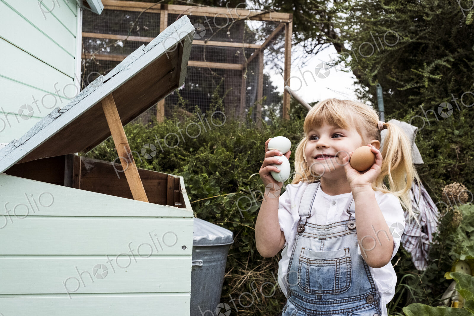 Smiling girl standing outdoors, holding three freshly laid eggs in her hands.