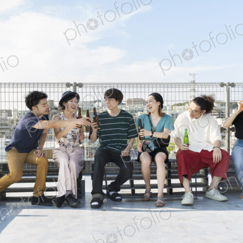 Smiling group of young Japanese men and women sitting on a rooftop in an urban setting. Smiling group of young Japanese men and women sitting on a rooftop in an urban setting.