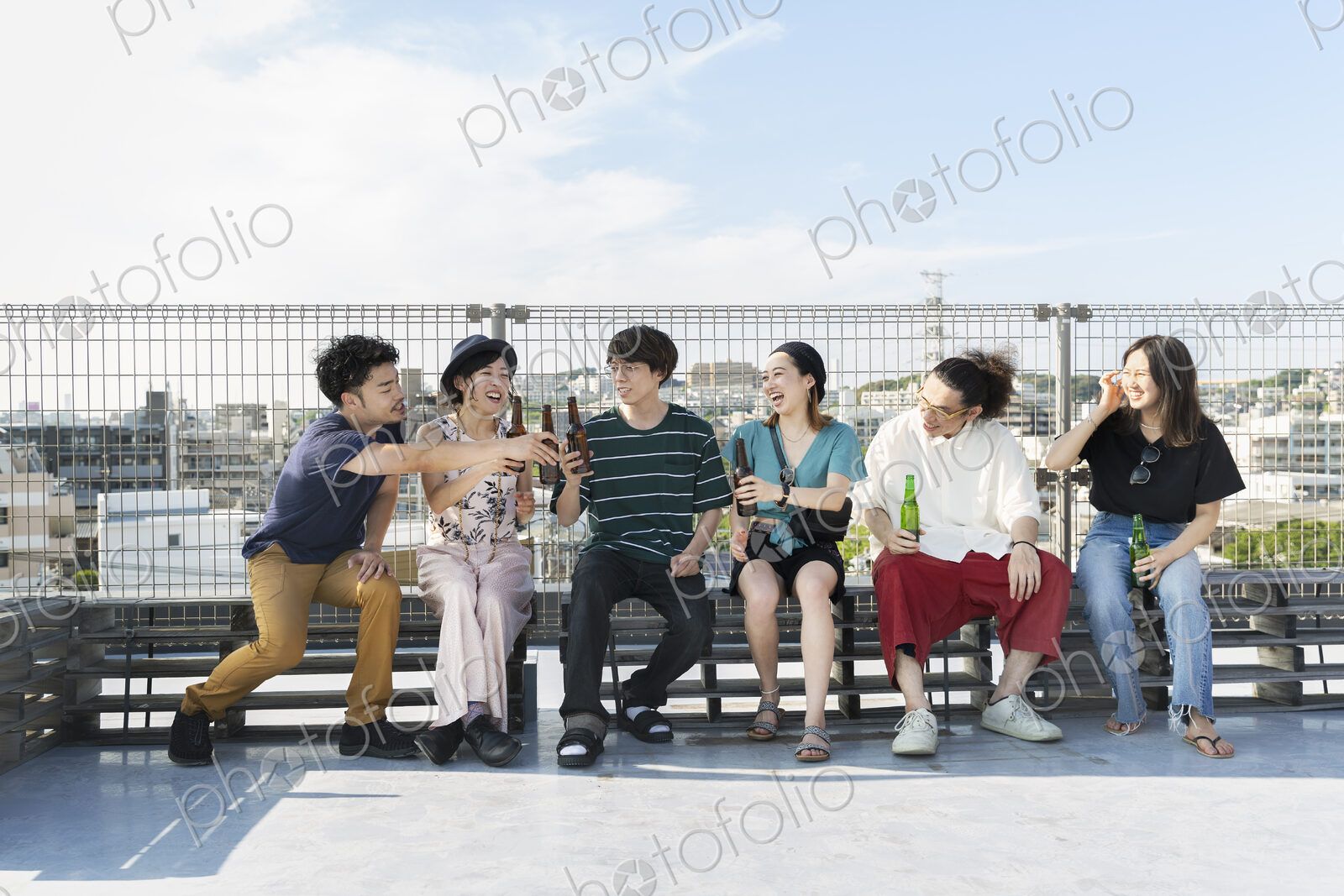 Smiling group of young Japanese men and women sitting on a rooftop in an urban setting.