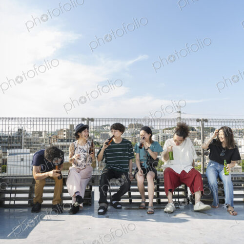 Smiling group of young Japanese men and women sitting on a rooftop in an urban setting. Smiling group of young Japanese men and women sitting on a rooftop in an urban setting.
