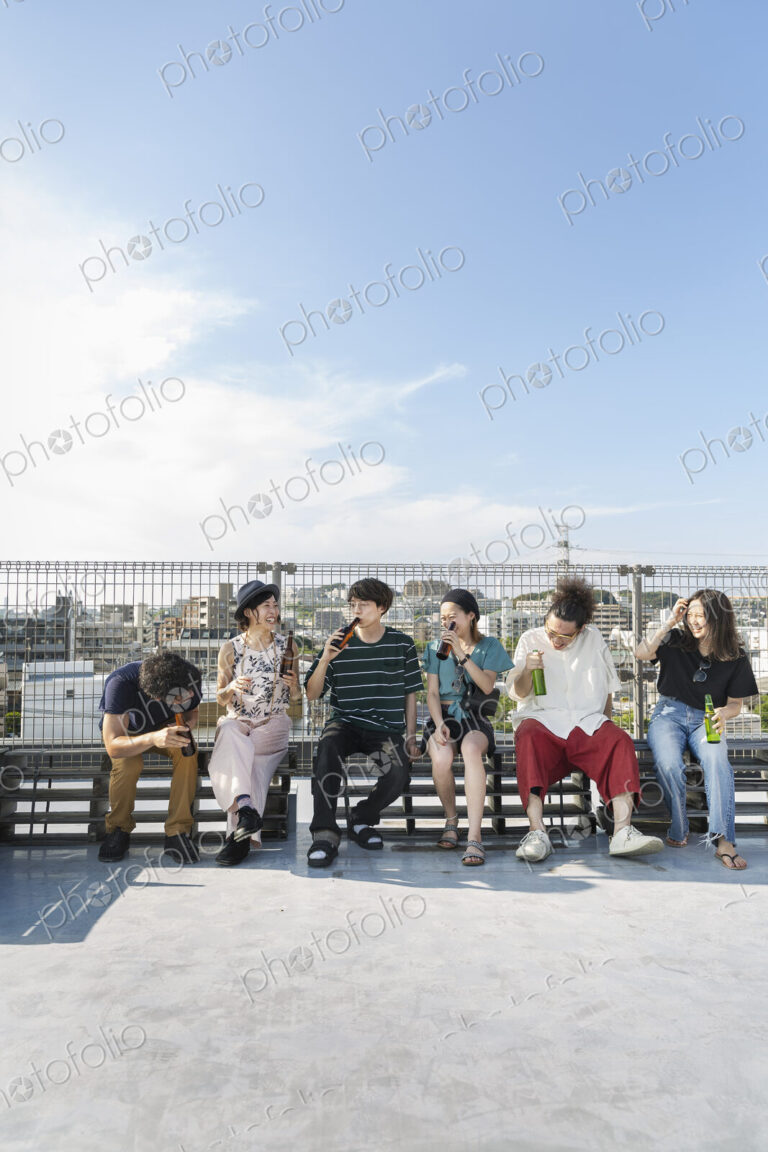 Smiling group of young Japanese men and women sitting on a rooftop in an urban setting.