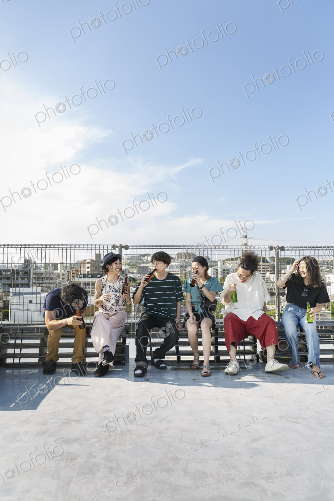 Smiling group of young Japanese men and women sitting on a rooftop in an urban setting.