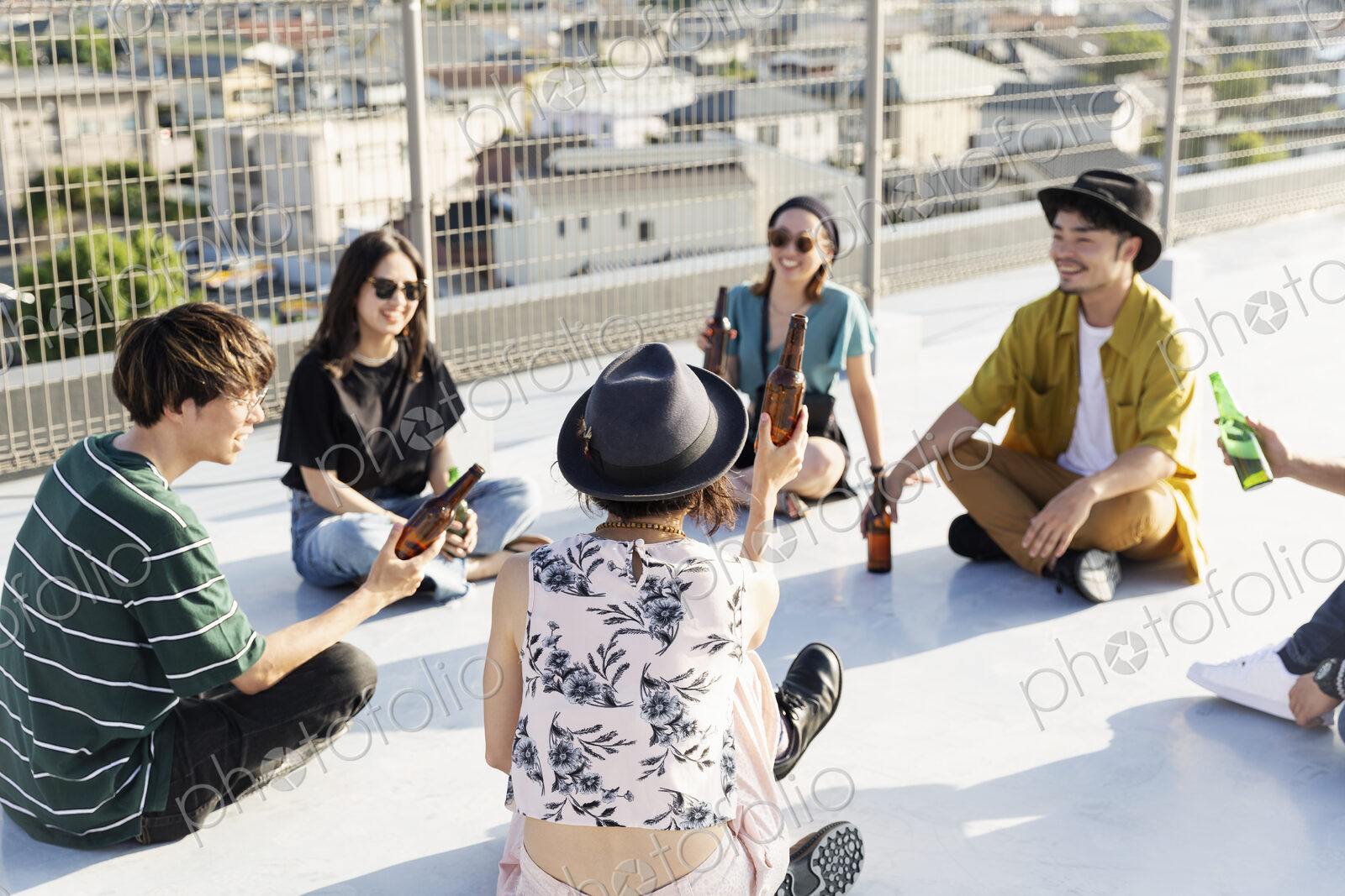 Smiling group of young Japanese men and women sitting on a rooftop in an urban setting.