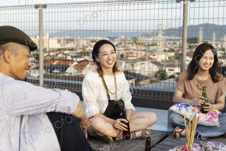 Smiling group of young Japanese men and women sitting on a rooftop in an urban setting.