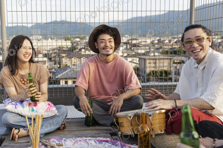Smiling group of young Japanese men and women sitting on a rooftop in an urban setting.