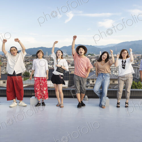 Smiling group of young Japanese men and women standing on a rooftop in an urban setting. Smiling group of young Japanese men and women standing on a rooftop in an urban setting.