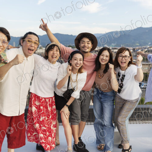 Smiling group of young Japanese men and women standing on a rooftop in an urban setting. Smiling group of young Japanese men and women standing on a rooftop in an urban setting.