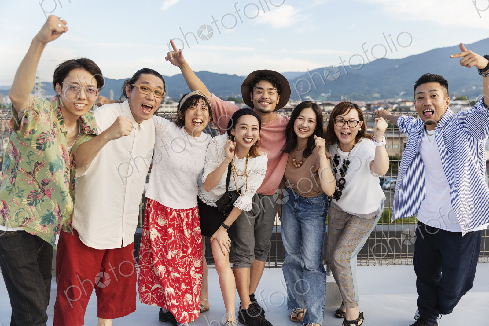 Smiling group of young Japanese men and women standing on a rooftop in an urban setting.