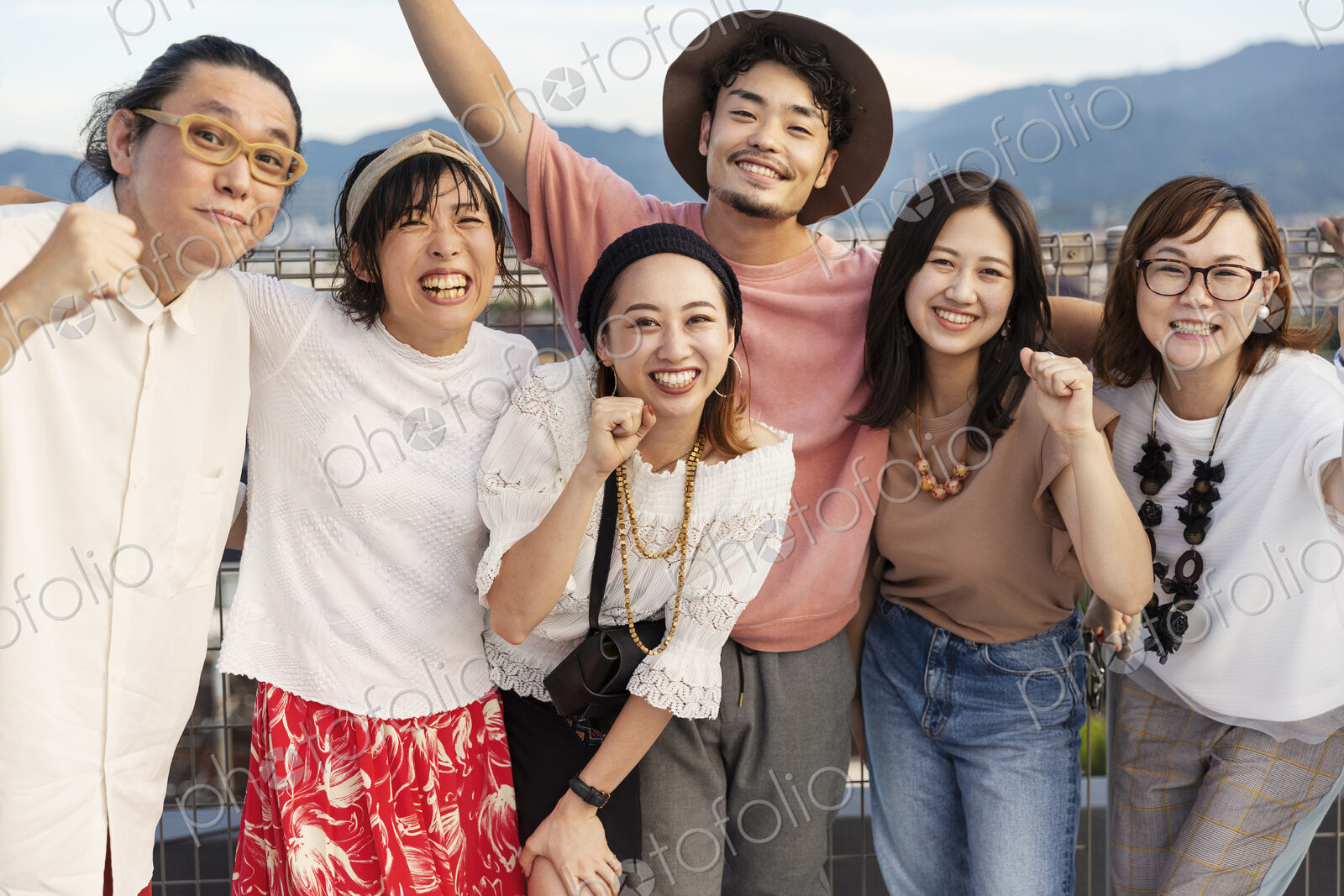 Smiling group of young Japanese men and women standing on a rooftop in an urban setting.