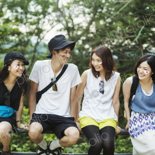 Smiling man and three young women sitting outdoors on a railing, faces painted with…