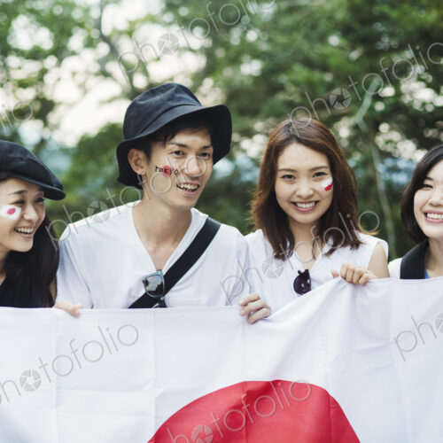 Smiling man and three young women standing outdoors, faces painted, holding Japanese flag. Smiling man and three young women standing outdoors, faces painted, holding Japanese flag.
