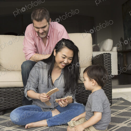 Smiling man and woman playing with their young son, building a wooden railway.