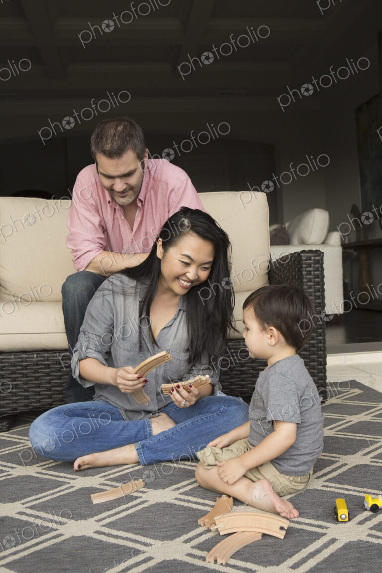 Smiling man and woman playing with their young son, building a wooden railway.