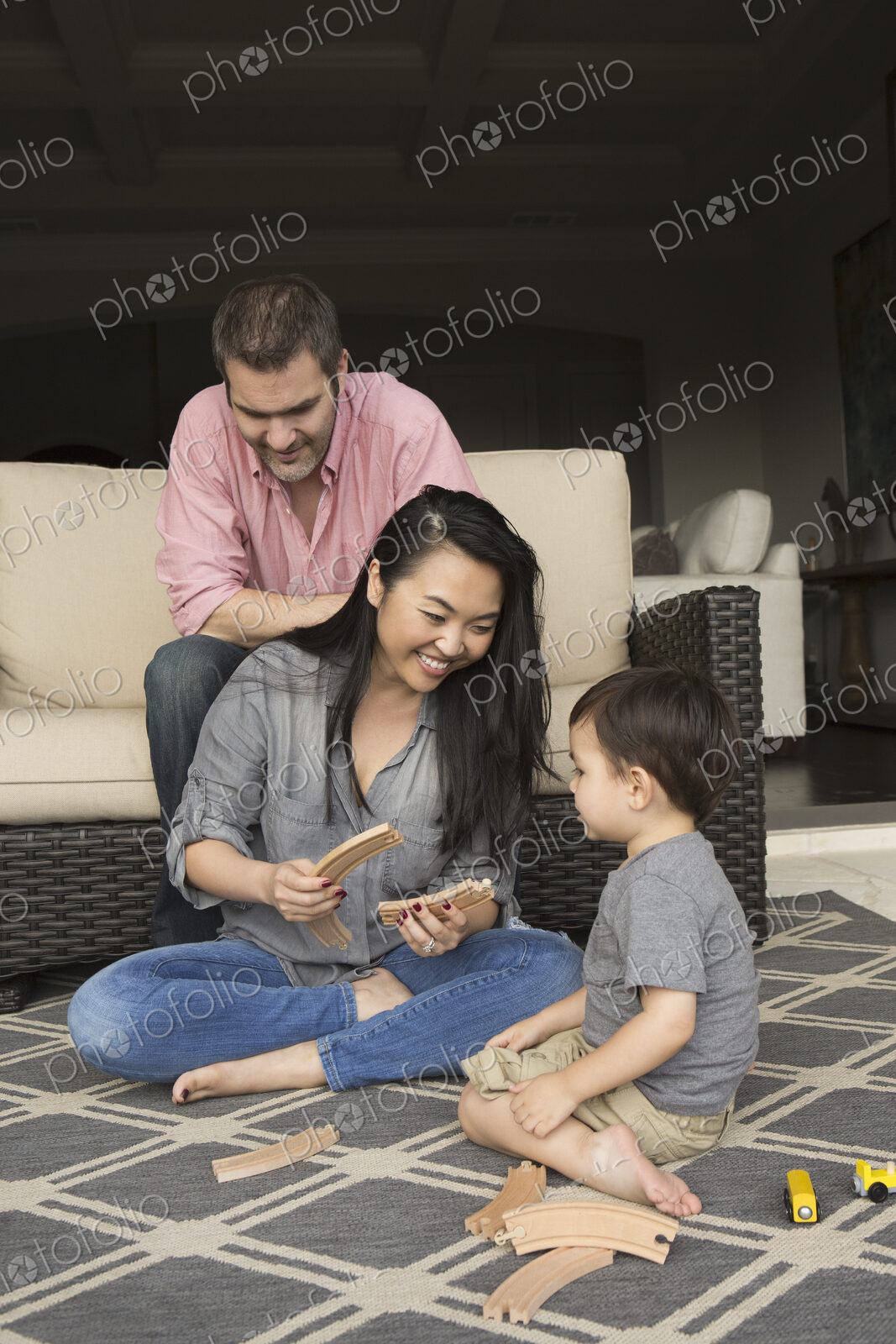 Smiling man and woman playing with their young son, building a wooden railway.