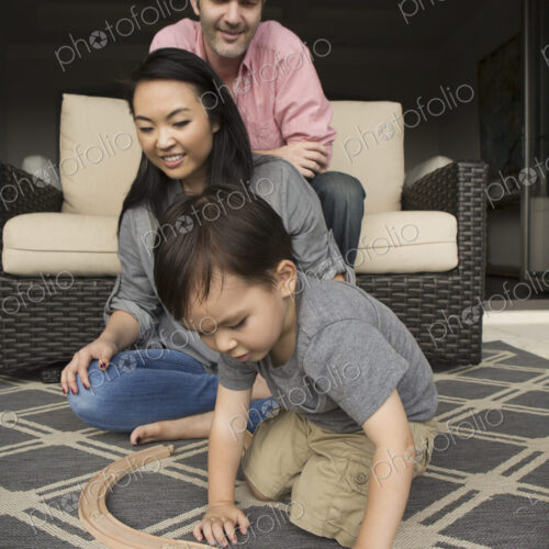 Smiling man and woman playing with their young son, building a wooden railway.