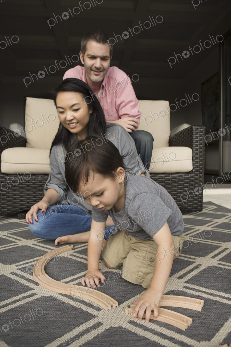 Smiling man and woman playing with their young son, building a wooden railway.