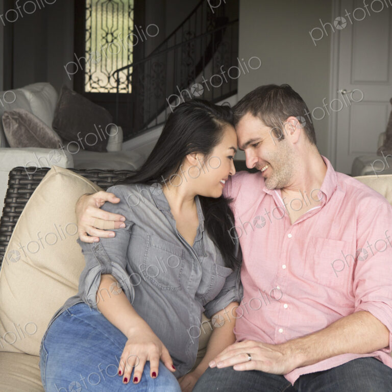 Smiling man and woman sitting on a sofa, hugging, and looking at each other.