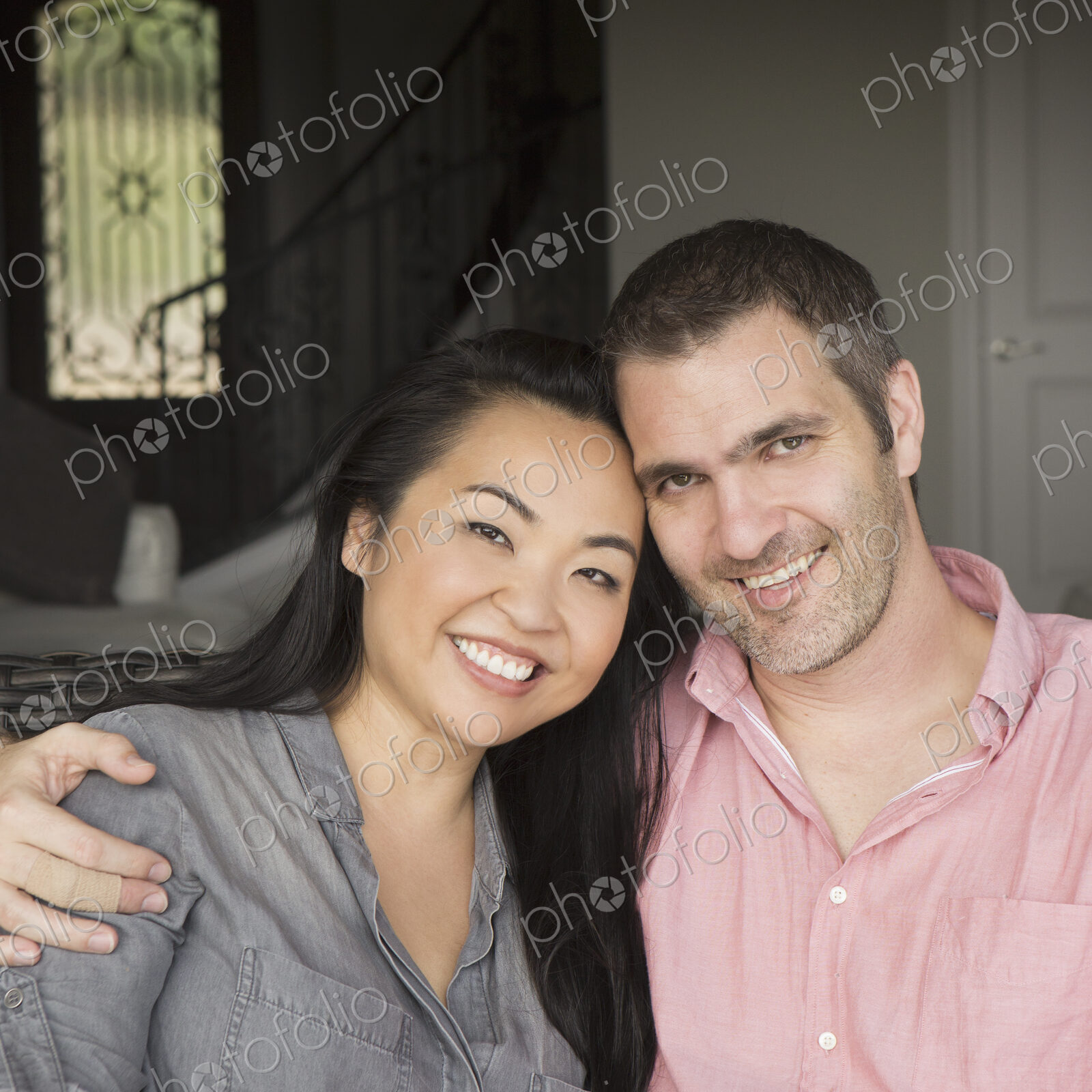 Smiling man and woman sitting on a sofa, hugging, and looking at the camera.