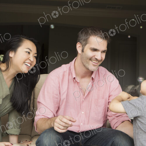Smiling man and woman sitting side by side on a sofa, playing with their young son. Smiling man and woman sitting side by side on a sofa, playing with their young son.
