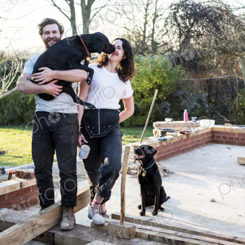 Smiling man and women and two black dogs on building site of residential building. Smiling man and women and two black dogs on building site of residential building.