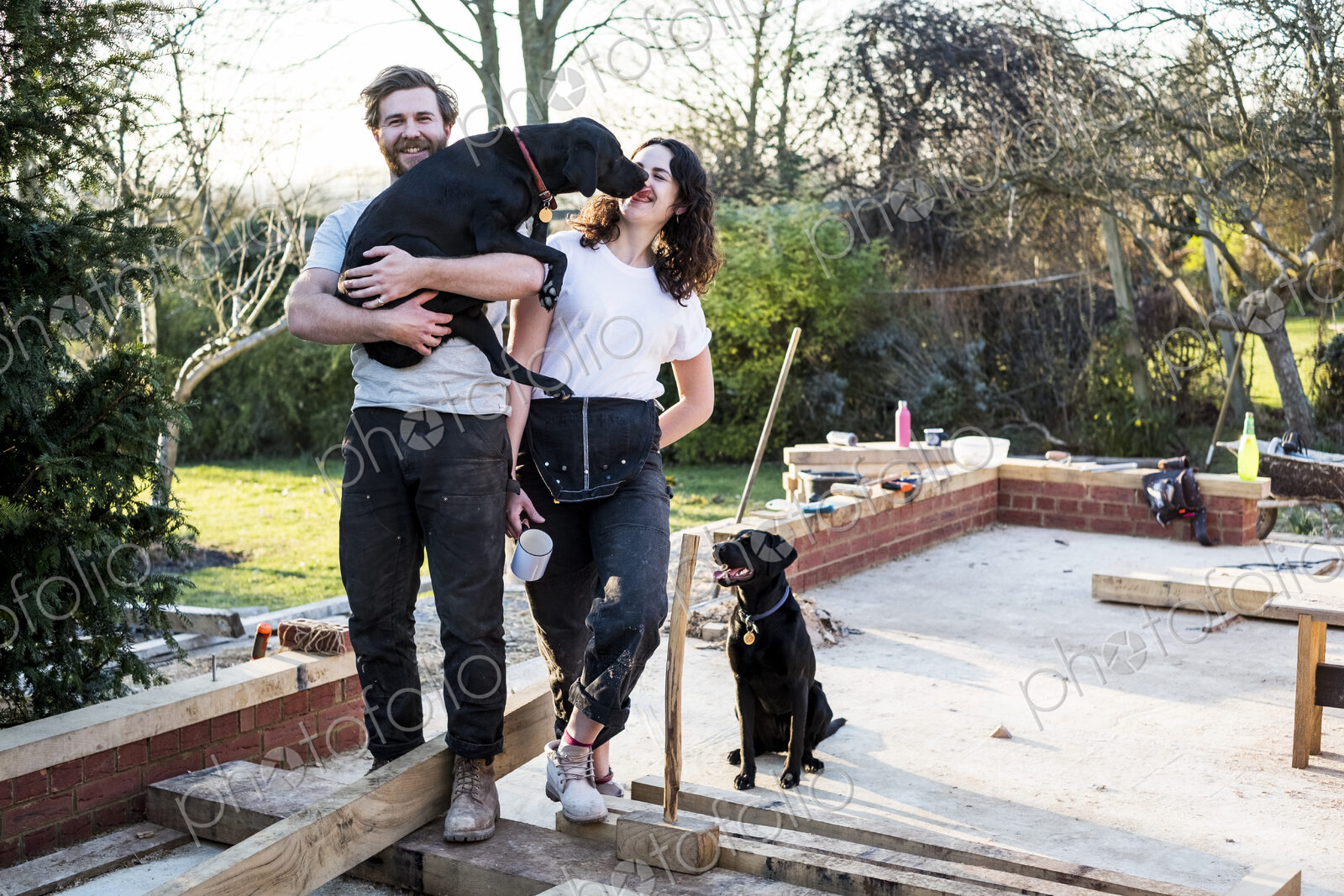 Smiling man and women and two black dogs on building site of residential building.