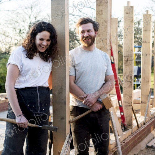 Smiling man and women holding hand tools standing on building site of residential… Smiling man and women holding hand tools standing on building site of residential…