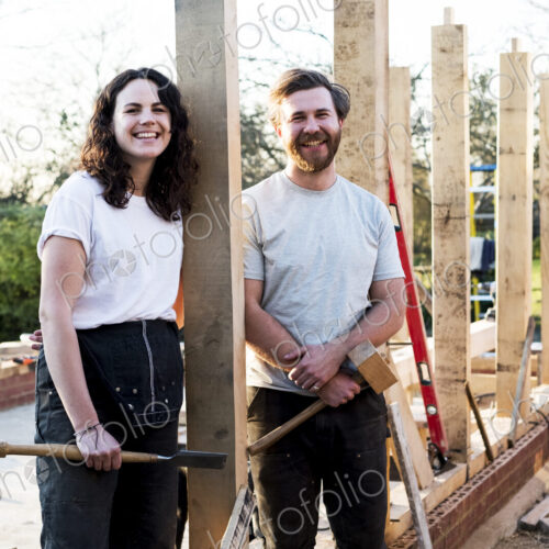 Smiling man and women holding hand tools standing on building site of residential… Smiling man and women holding hand tools standing on building site of residential…