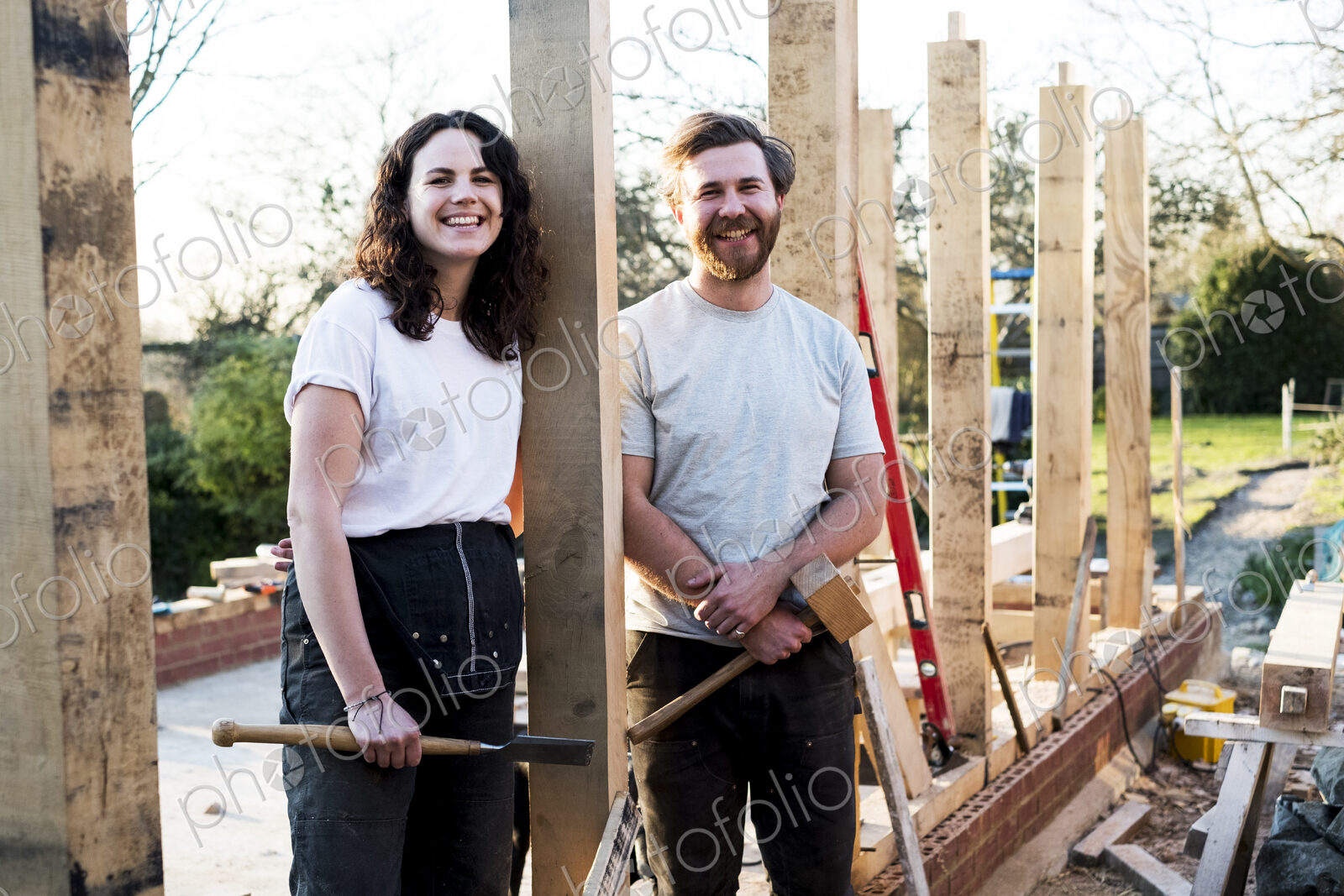 Smiling man and women holding hand tools standing on building site of residential…