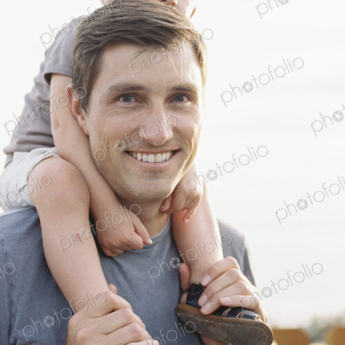 Smiling man carrying his young son on his shoulders. Smiling man carrying his young son on his shoulders.
