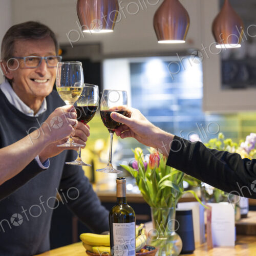 Smiling man drinking red wine with friends in kitchen.