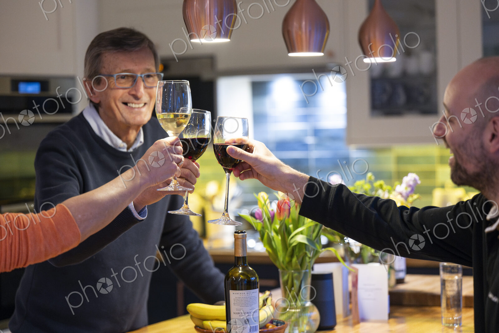 Smiling man drinking red wine with friends in kitchen.