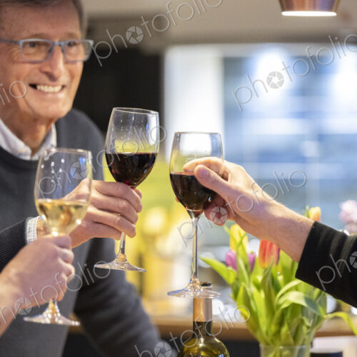Smiling man drinking red wine with friends in kitchen.