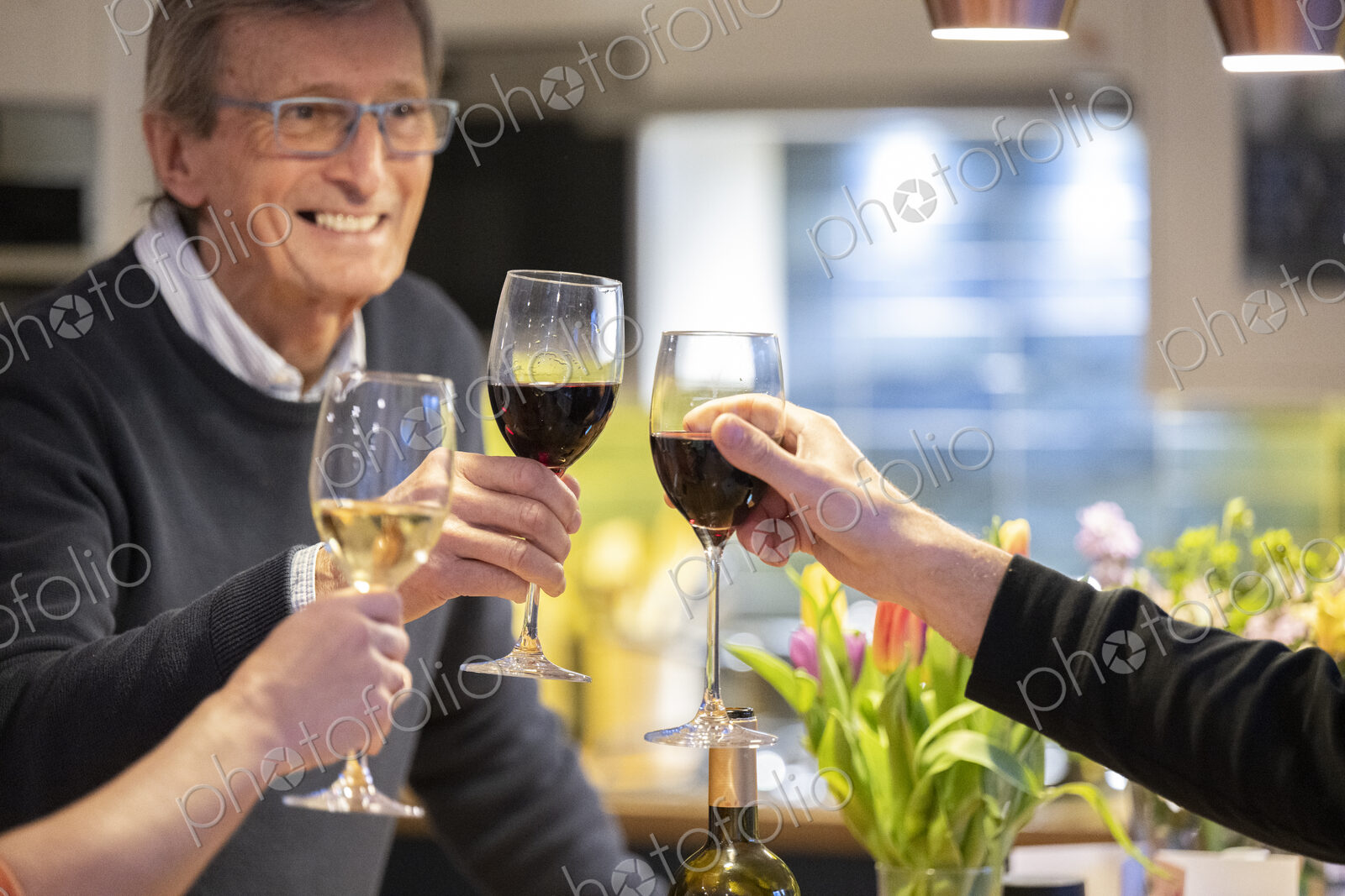 Smiling man drinking red wine with friends in kitchen.