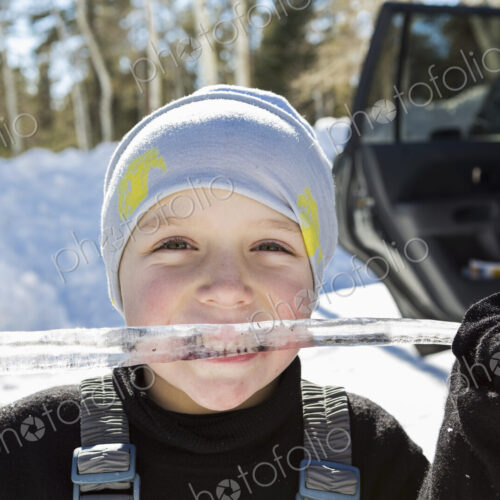 Smiling six year old boy with a long icicle in his mouth