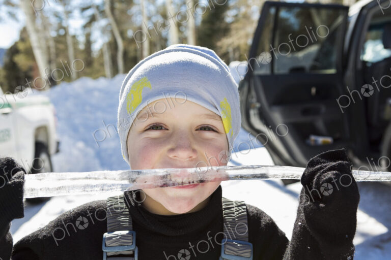 Smiling six year old boy with a long icicle in his mouth