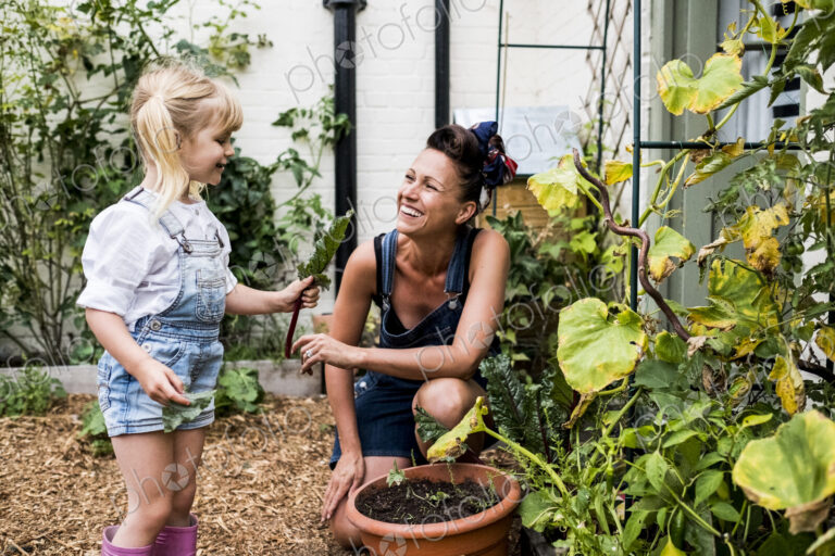 Smiling woman and girl in a garden, picking fresh vegetables.