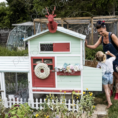 Smiling woman and girl standing in a garden next to a colourful hen house.