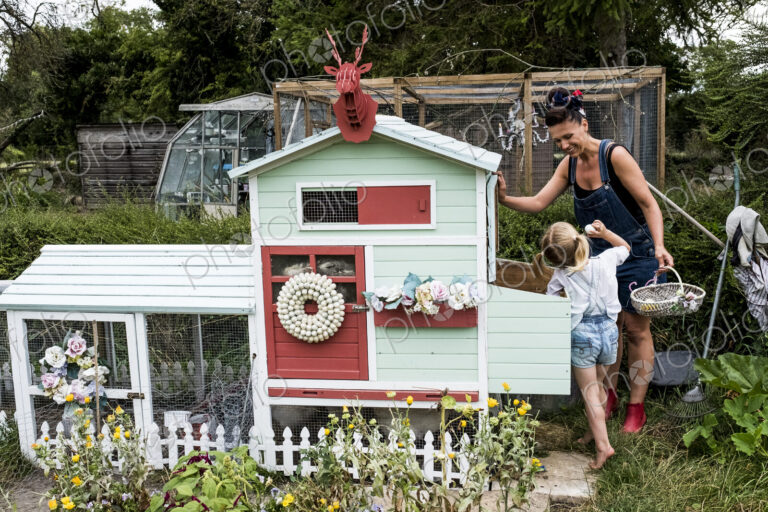 Smiling woman and girl standing in a garden next to a colourful hen house.