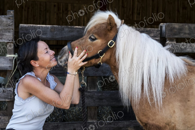 Smiling woman holding a Shetland pony with a long blonde mane by its bridle.