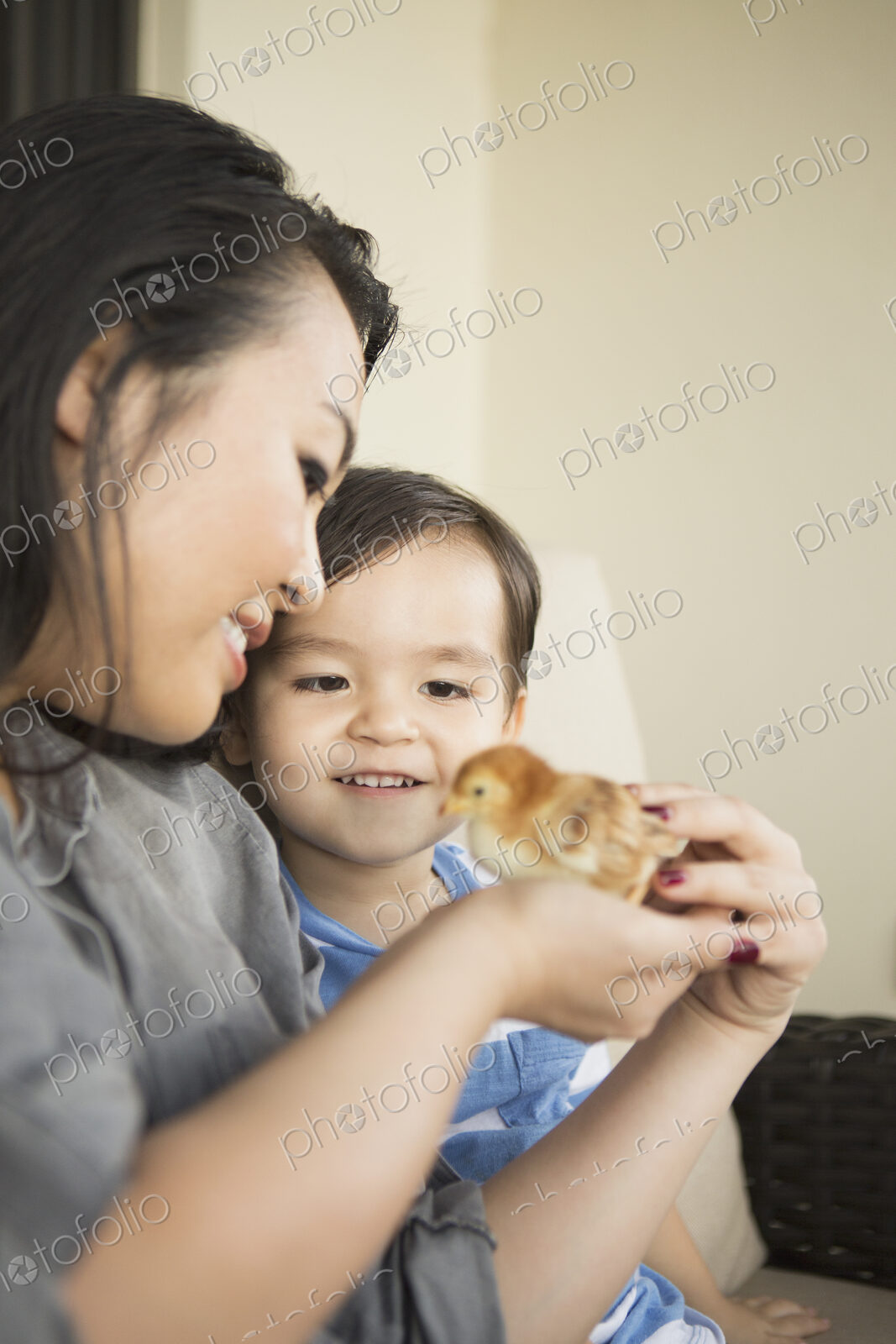 Smiling woman holding a tiny chick in her hands, her young son watching.