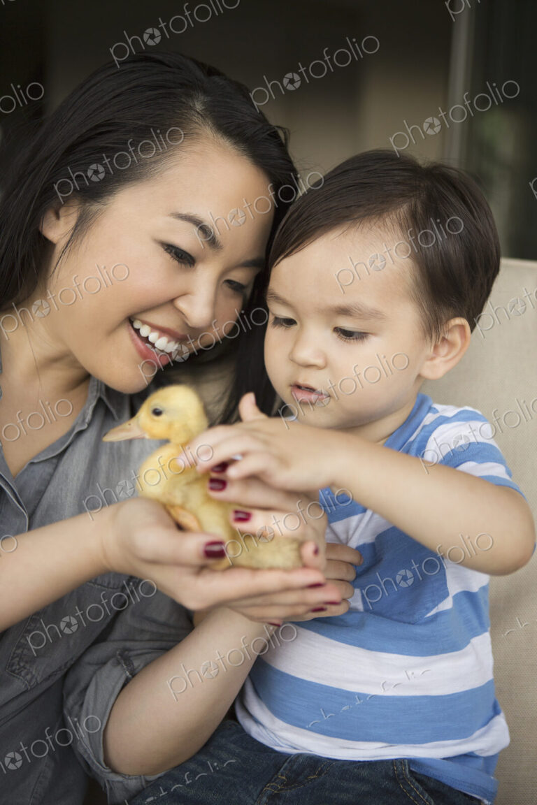 Smiling woman holding a yellow duckling in her hands, her young son stroking the animal.