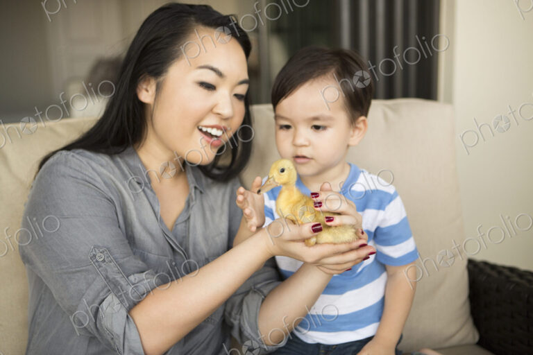 Smiling woman holding a yellow duckling in her hands, her young son watching.